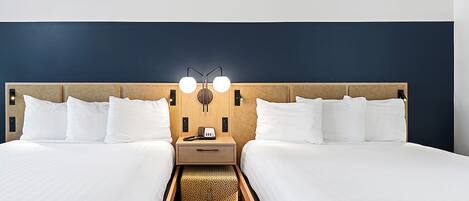 A hotel room with two beds, a nightstand with a lamp, and a small table.