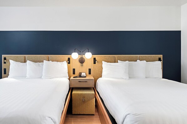 A hotel room with two beds, a nightstand with a lamp, and a small table.