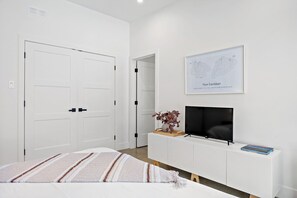 A modern bedroom with a bed, a TV on a white console, a framed botanical print, and a door. - Rockhaus-Cliffside Dome Sauna/Hot Tub/Tremblant (La Conception)