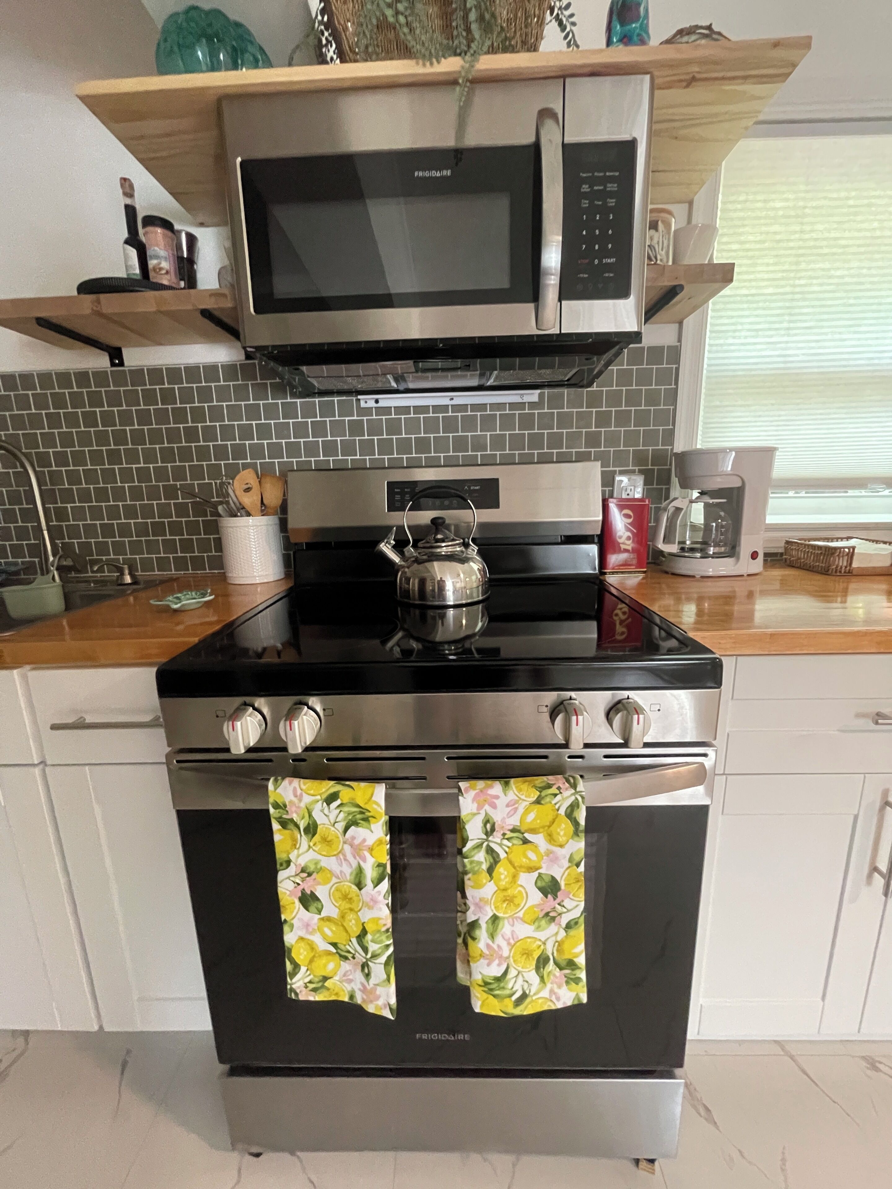 A kitchen with a stainless steel stove, a microwave above it, and a kettle on the stove.