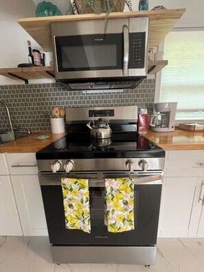Een keuken met een roestvrijstalen fornuis, een magnetron erboven en een waterkoker op het fornuis.