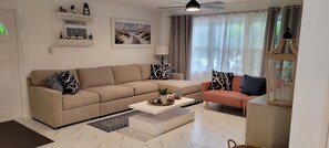 A living room with a beige sofa, a smaller pink sofa, a coffee table, and a glass cabinet with decorative items. - “No worries “ (Pompano Beach)