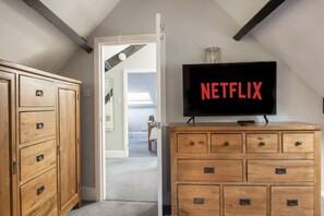A room with a wooden dresser, a television displaying 'NETFLIX,' and a door leading to another room. - Beautiful Secluded 2 Bedroom Coach House (Nottingham)