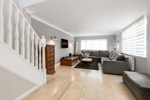 A living room with a grey sofa, wooden cabinet, and a staircase with white balusters. - Beautiful Secluded 2 Bedroom Coach House (Nottingham)
