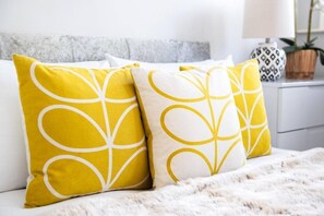 A bed with two pillows featuring a leaf pattern, a fluffy white blanket, and a bedside table with a lamp and a potted plant. - Luxury 2 Bedroom Apartment in The Park Estate (Nottingham)