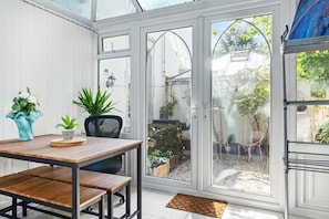 A conservatory with a wooden table and chairs, potted plants, and a view of the garden outside. - Luxury 2 Bedroom Apartment in The Park Estate (Nottingham)