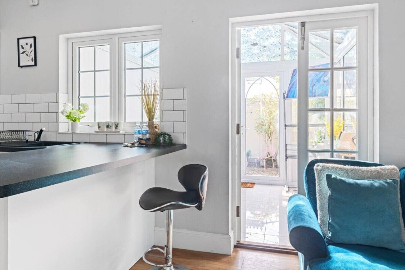 Eine moderne Küche mit Bar, einem Essbereich mit blauem Sofa und Blick ins Freie durch große Fenster.