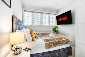 Ein modernes Hotelzimmer mit einem Bett, einem an der Wand befestigten Fernseher und einem Fenster mit Jalousien.