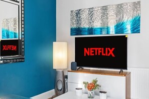 A room with a large flat-screen TV displaying the Netflix logo, a lamp, and a framed artwork above the TV. - Luxury 2 Bedroom Apartment in The Park Estate (Nottingham)