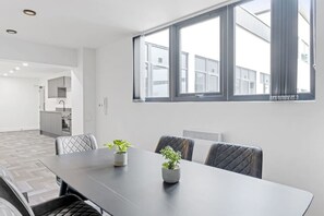 Ein modernes Interieur mit einem Esstisch, Stühlen, Topfpflanzen und einem großen Fenster.