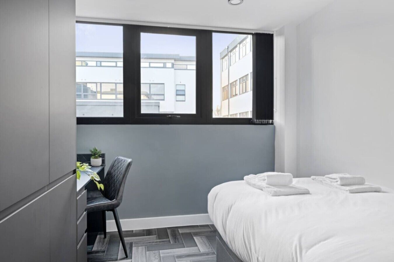 A hotel room with a bed, a desk, a chair, and a window with a view of buildings.