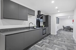 A modern kitchen with grey cabinetry, a black sink, and a herringbone-patterned floor. - Brand New Spacious Studio in Beeston (Beeston)