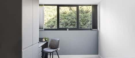 Un dormitorio con cama, escritorio y silla. Se ve una ventana con vistas a árboles.