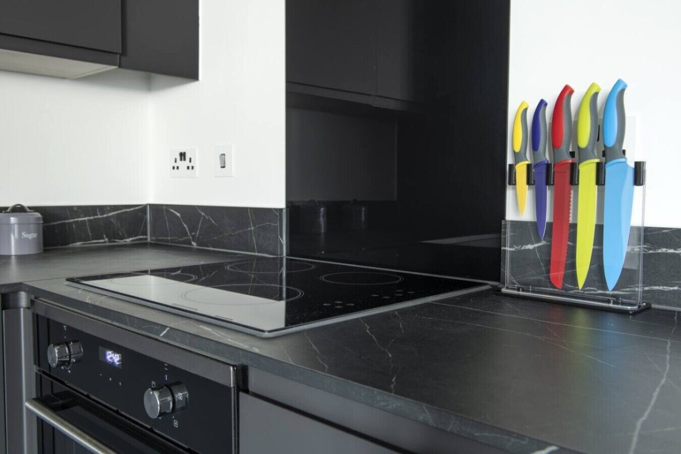 Cocina moderna con encimera negra, estufa integrada y bloque de cuchillos con mangos de colores.