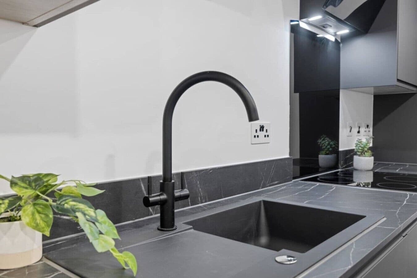 Eine moderne Küche mit einem schwarzen Spülbecken, einem gebogenen Wasserhahn und einer Marmorarbeitsplatte.