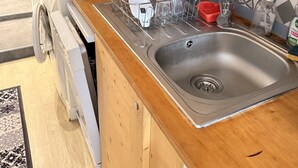 Keittiössä on puiset kaapit, ruostumattomasta teräksestä valmistettu pesuallas ja astiateline.