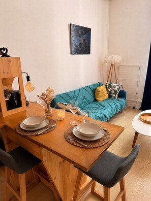 A dining area with a wooden table, chairs, and a blue sofa in the background. - Le cocon des Capucins (Lyon)
