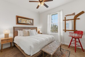 A bedroom with a bed, bedside tables, a red chair, a window with blinds, and a ceiling fan. - Tranquil Tides (New Smyrna Beach)