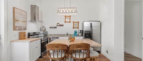 Una cocina con armarios blancos, una mesa de comedor de madera y cuatro sillas de mimbre.