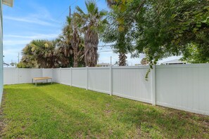 A fenced backyard with a bench and grass. - Tranquil Tides (New Smyrna Beach)