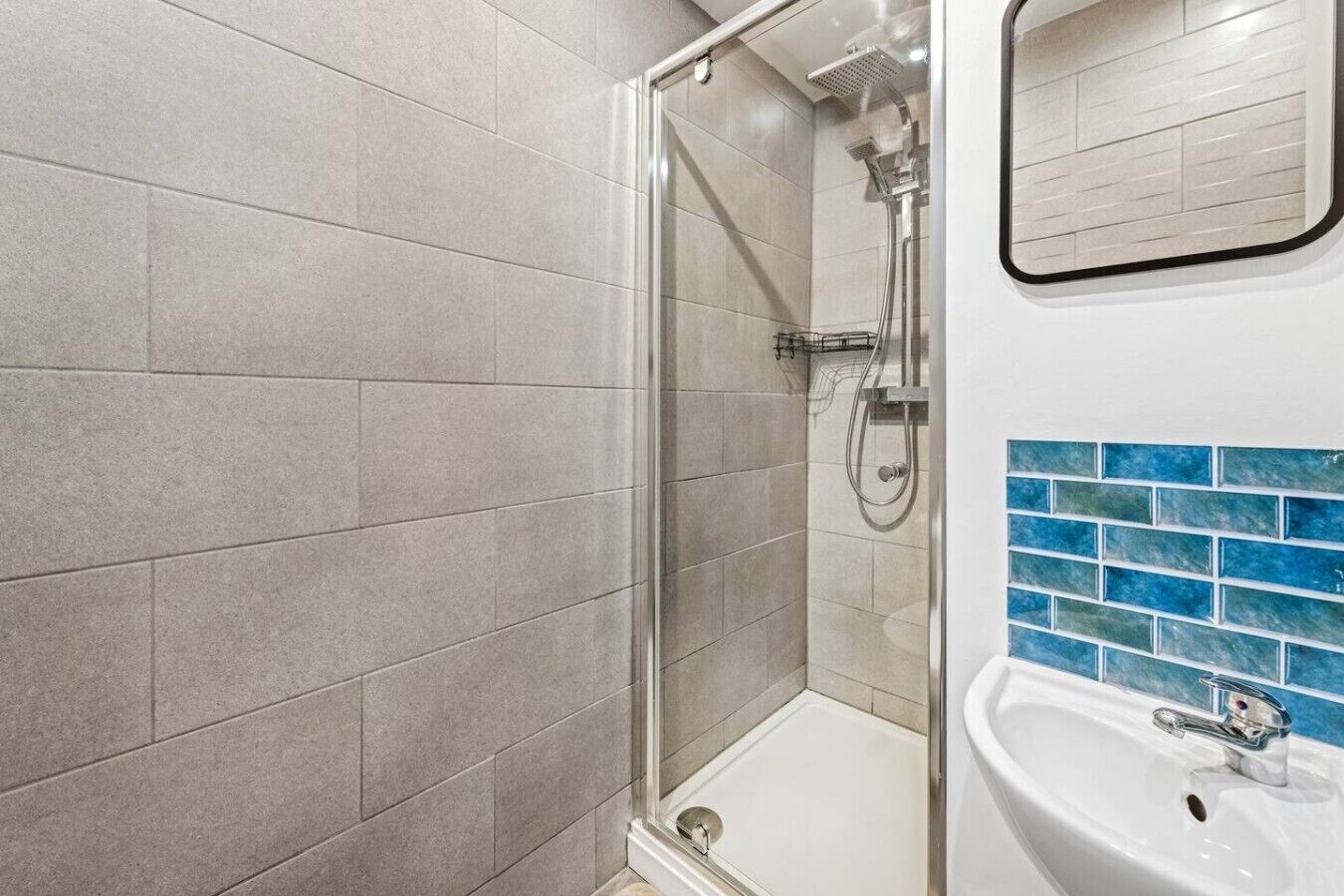 A bathroom with a glass-enclosed shower, a white sink, and blue-tiled walls.