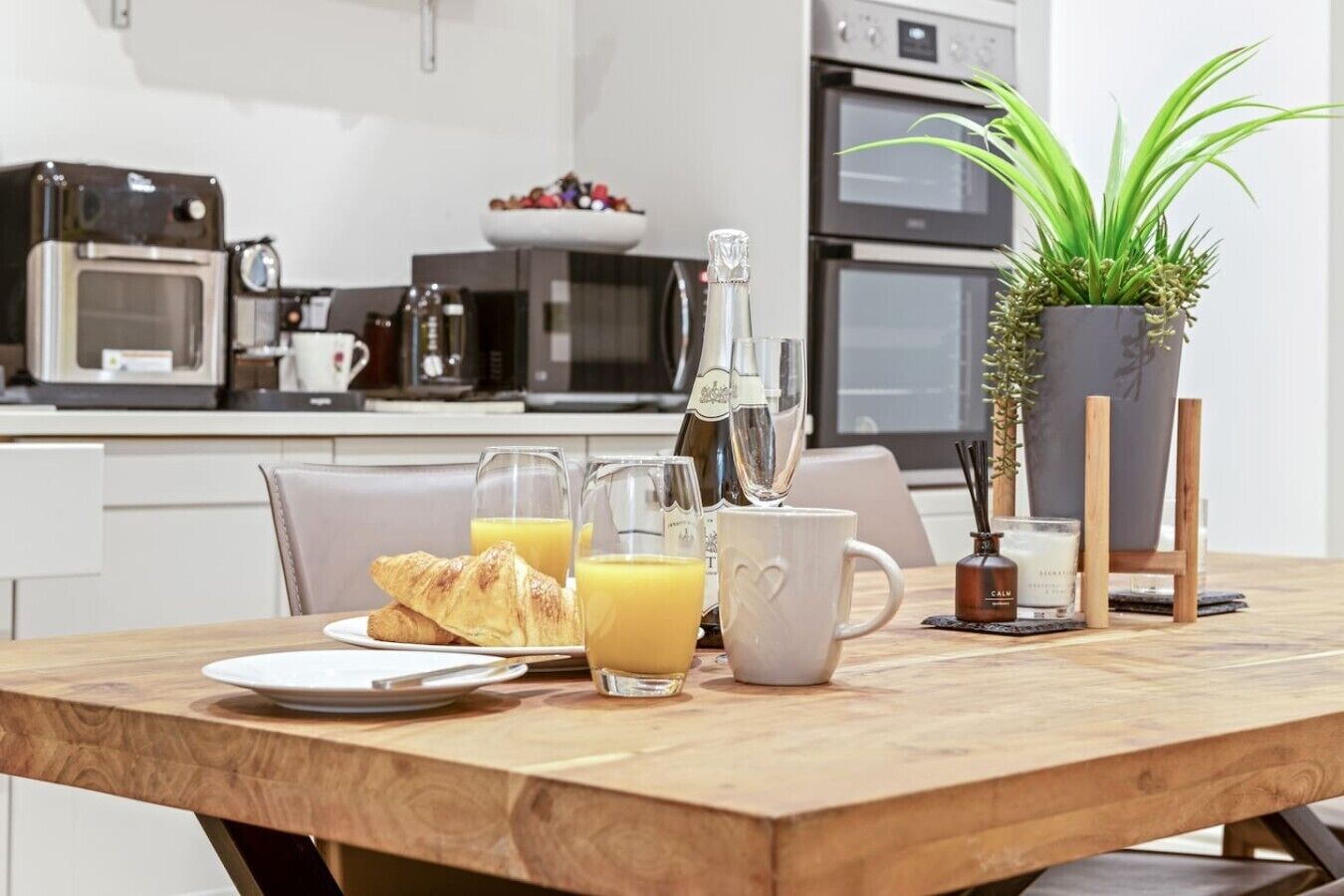 Une table en bois dressée pour le petit-déjeuner, avec des croissants, du jus d’orange et des coupes à champagne.
