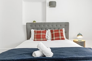 A neatly made bed with a blue blanket, two red and white pillows, and a white towel. - Luxurious 3 Bedroom Apartment in Park Estate (Nottingham)