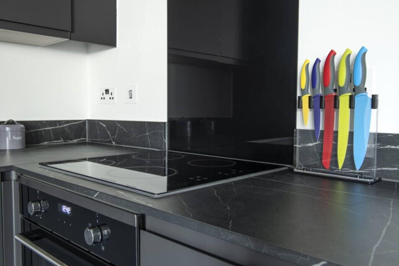 Une cuisine moderne avec un plan de travail noir, une cuisinière encastrée et un bloc à couteaux doté de manches colorées.