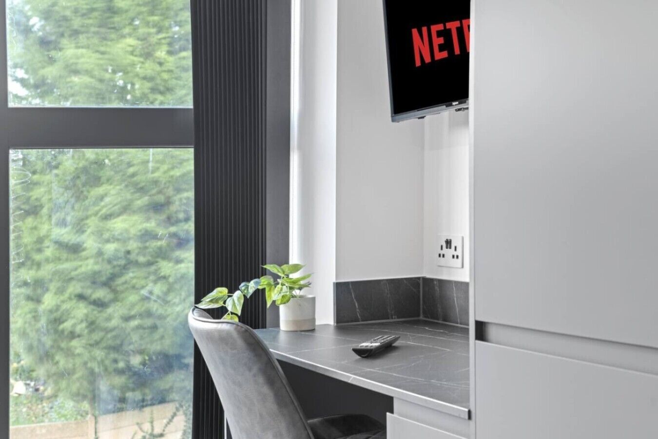 Una cocina moderna con un ventanal grande, una planta en la encimera y un televisor de pantalla plana montado sobre la encimera.