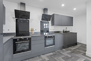 A modern kitchen with a central island, built-in ovens, and a large grey cabinet above the countertop. - Brand New Spacious Studio in Beeston (Beeston)