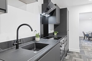 A modern kitchen with a black sink, stainless steel appliances, and a herringbone-patterned floor.