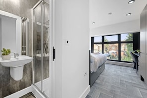 A modern bathroom with a glass shower enclosure, a white sink, and a potted plant.