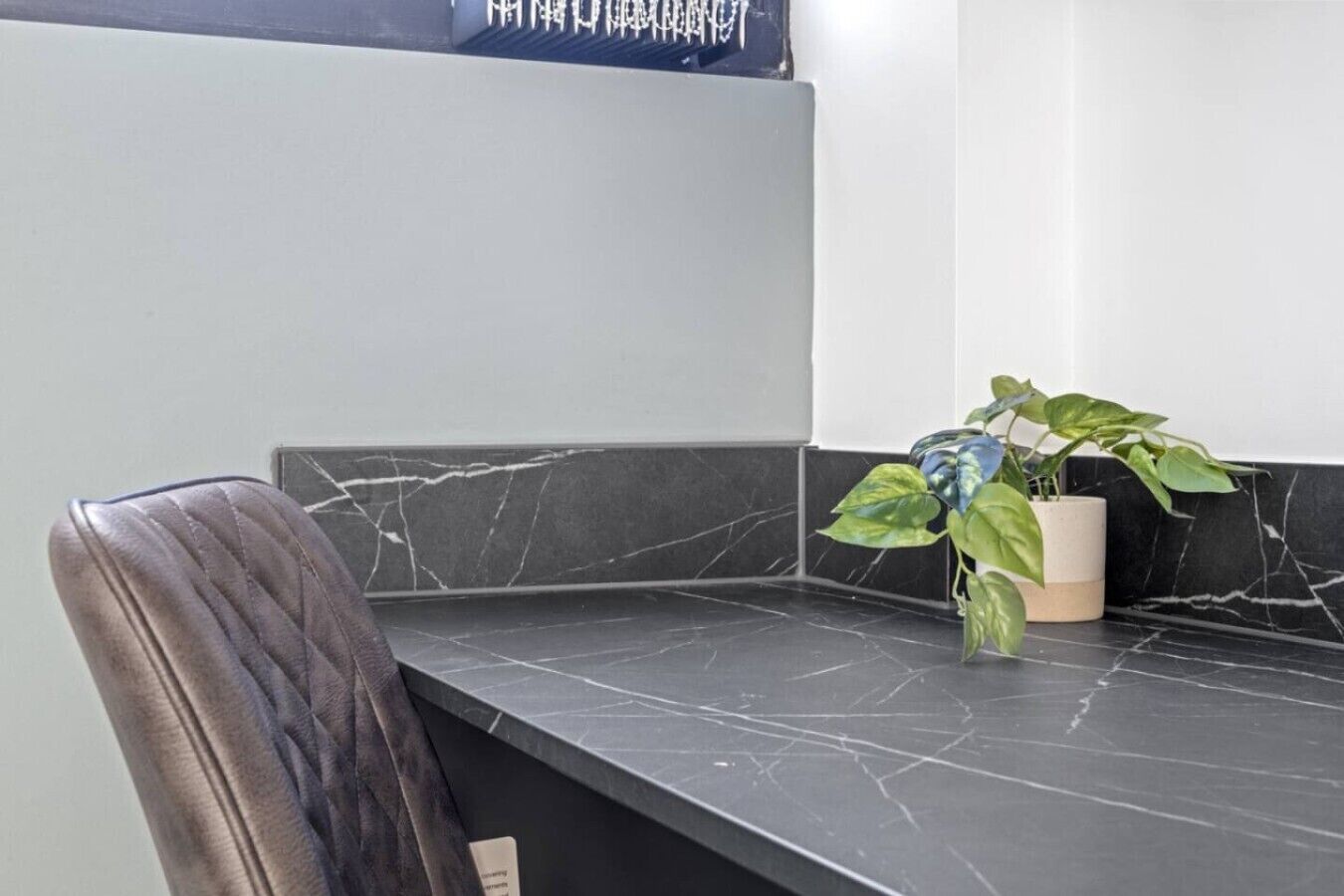 Un coin de pièce avec un plan de travail en marbre foncé, une plante en pot et une chaise.