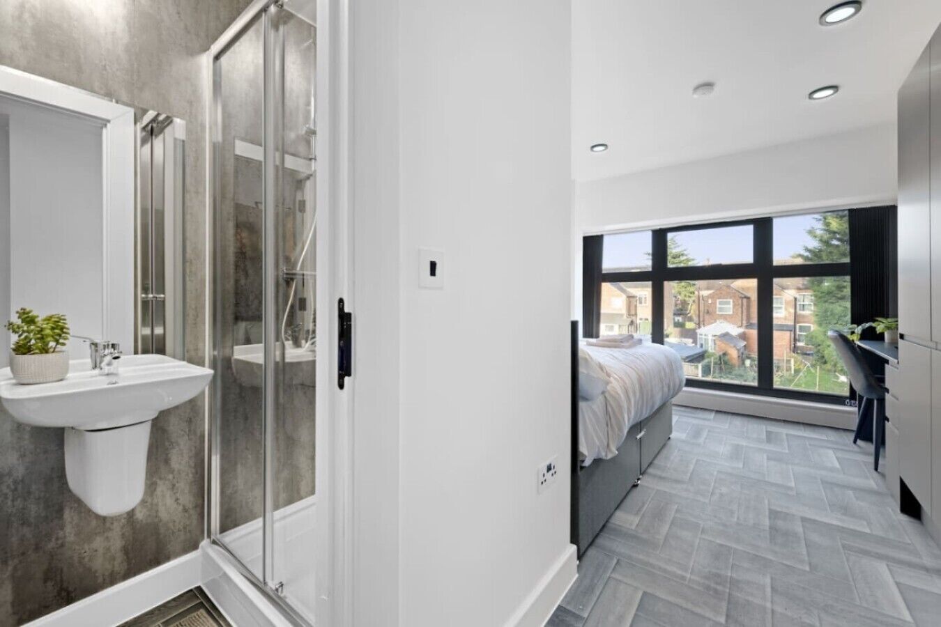 A modern bathroom with a glass shower enclosure, a white sink, and a potted plant.