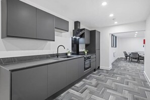 A modern kitchen with grey cabinets, a black sink, and a herringbone-patterned floor. - Brand New Spacious Studio in Beeston (Beeston)