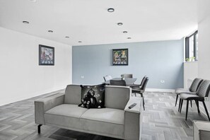 A modern living room with a grey sofa, a dining table with chairs, and artwork on the walls. - Brand New Spacious Studio in Beeston (Beeston)