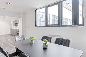 A modern interior with a dining table, chairs, potted plants, and a view of the outside through large windows.