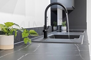 A modern kitchen with a sleek black faucet, a marble countertop, and a potted plant.