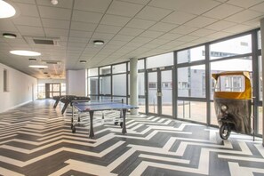 A spacious indoor area with a ping pong table and a scooter, large windows, and a patterned floor.