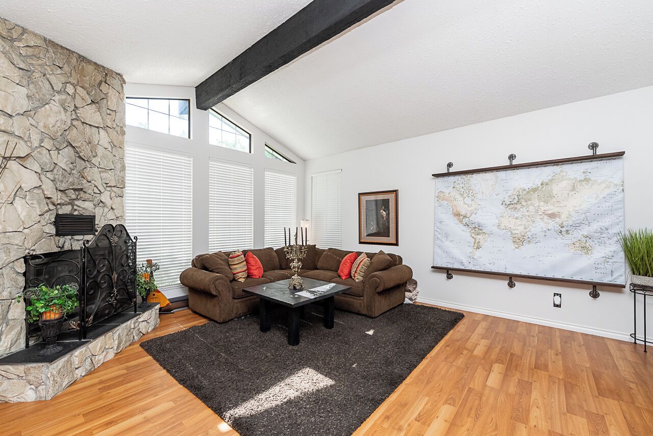 Un salon avec une cheminée en pierre, un canapé d’angle, une table basse et une carte du monde accrochée au mur.