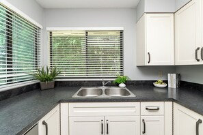 A kitchen with a double sink, white cabinets, and a window with blinds. - East Abbotsford Spanish Villa (Abbotsford)