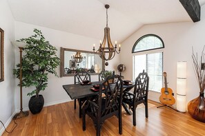 A dining area with a wooden table, dark chairs, a chandelier, a potted plant, a guitar, and a mirror on the wall. - East Abbotsford Spanish Villa (Abbotsford)