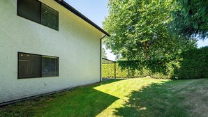 A modern two-story building with a white exterior, a well-maintained lawn, and a large tree providing shade. - East Abbotsford Spanish Villa (Abbotsford)