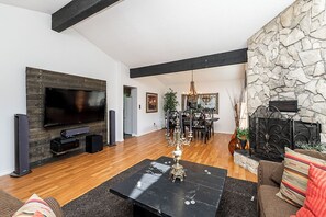 A modern living room with a flat-screen TV, a fireplace, and a dining area with a chandelier. - East Abbotsford Spanish Villa (Abbotsford)