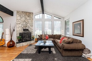 A living room with a stone fireplace, a large window, a sofa, and a coffee table. - East Abbotsford Spanish Villa (Abbotsford)