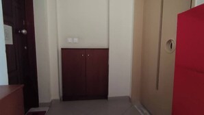 A hallway with a wooden door, a red door, and a light switch on the wall.