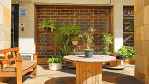 Un banco de madera y una mesa redonda con plantas en macetas en un patio con pared de ladrillo y puerta de madera.