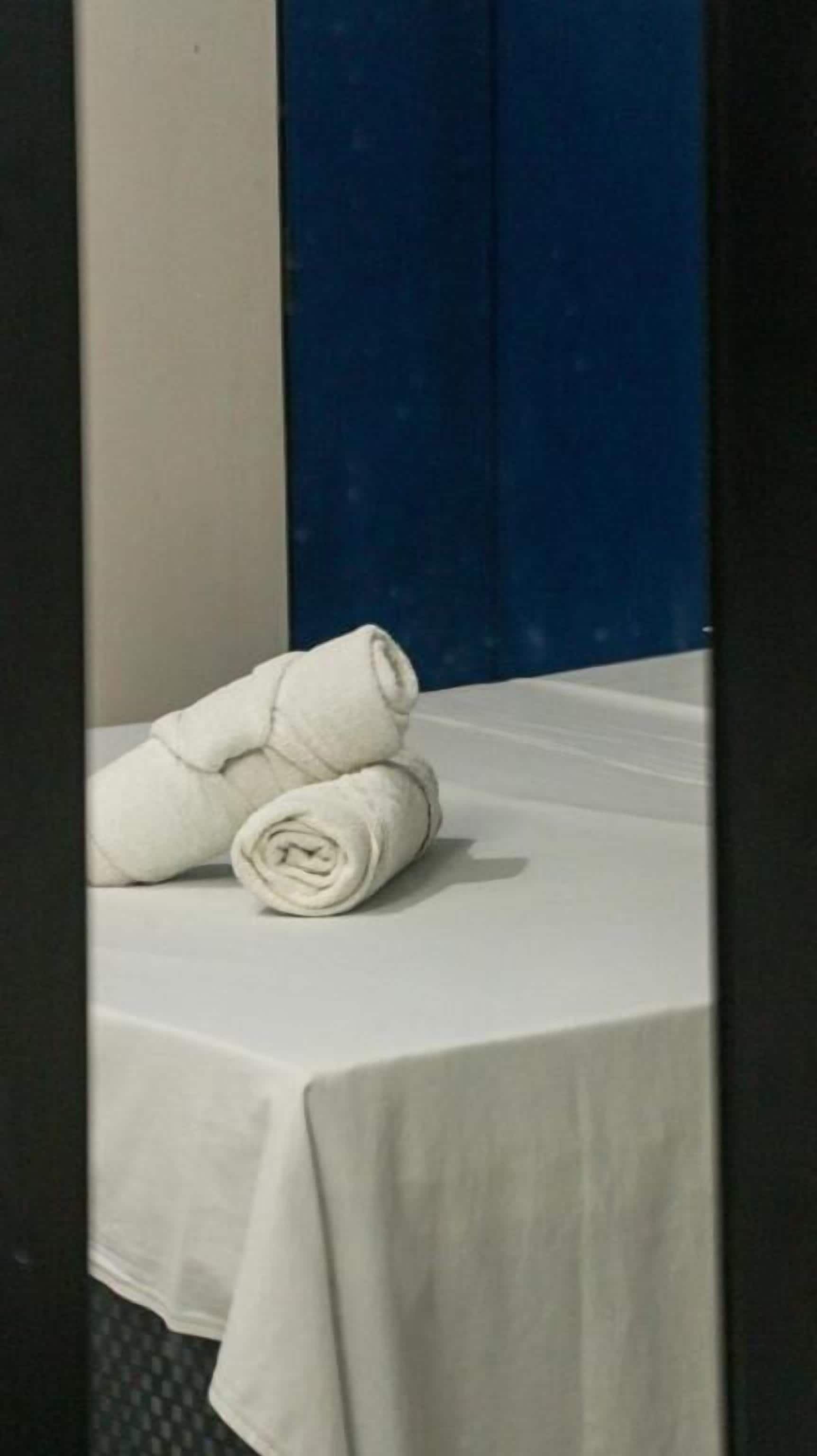 A room with a bed covered by a white sheet, a blue curtain, and a folded white towel on the bed.