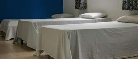 Habitación de hotel con tres camas individuales, una pared azul y una ventana con cortinas.