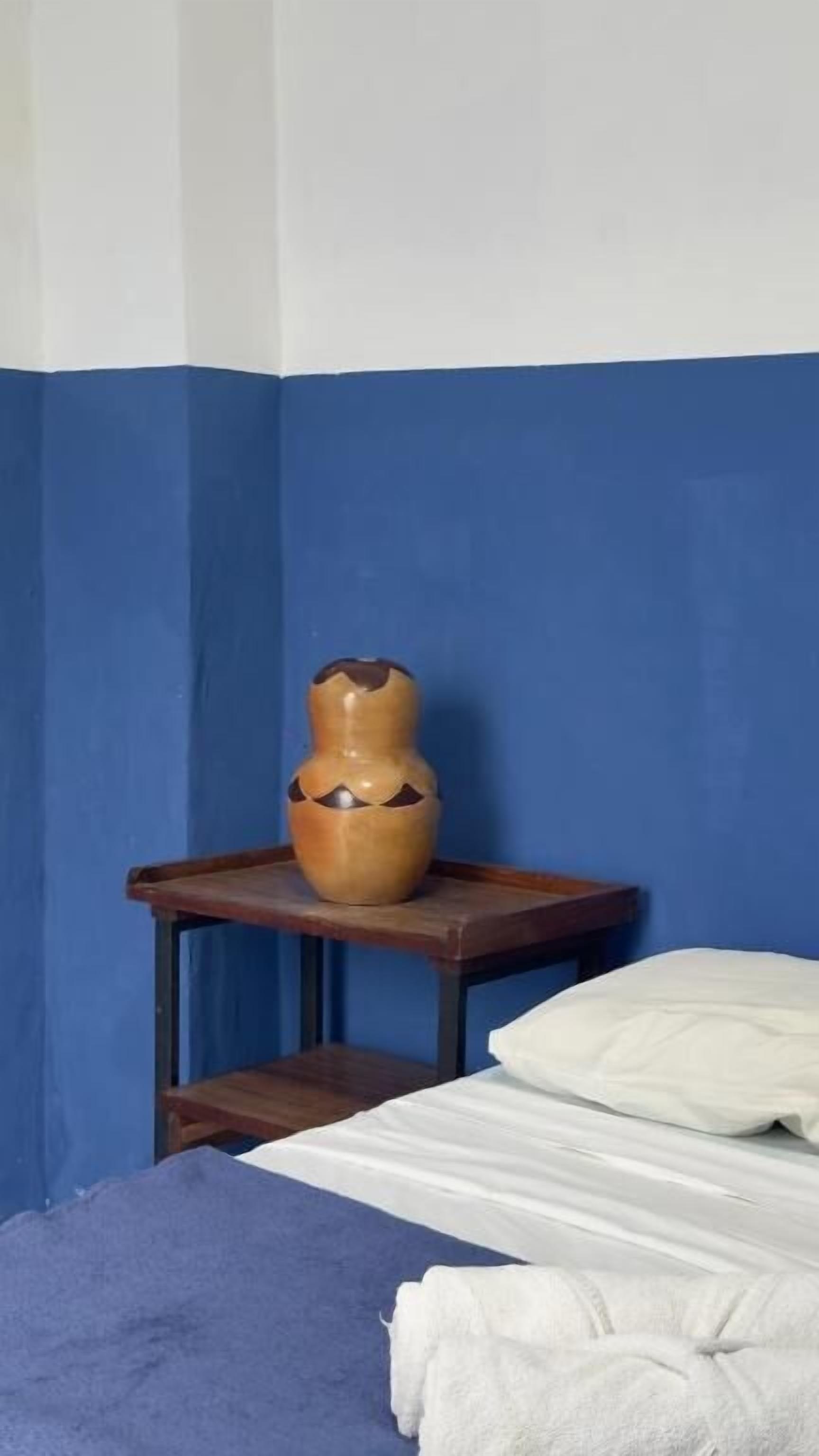 Ein Zimmer mit einem Bett, einem kleinen Tisch mit einer Vase und einer blauen Wand.